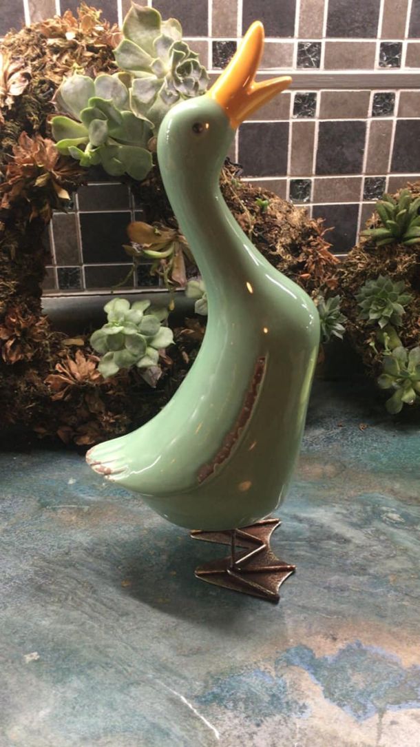 A ceramic green goose with a flowery wreath in behind on the kitchen table